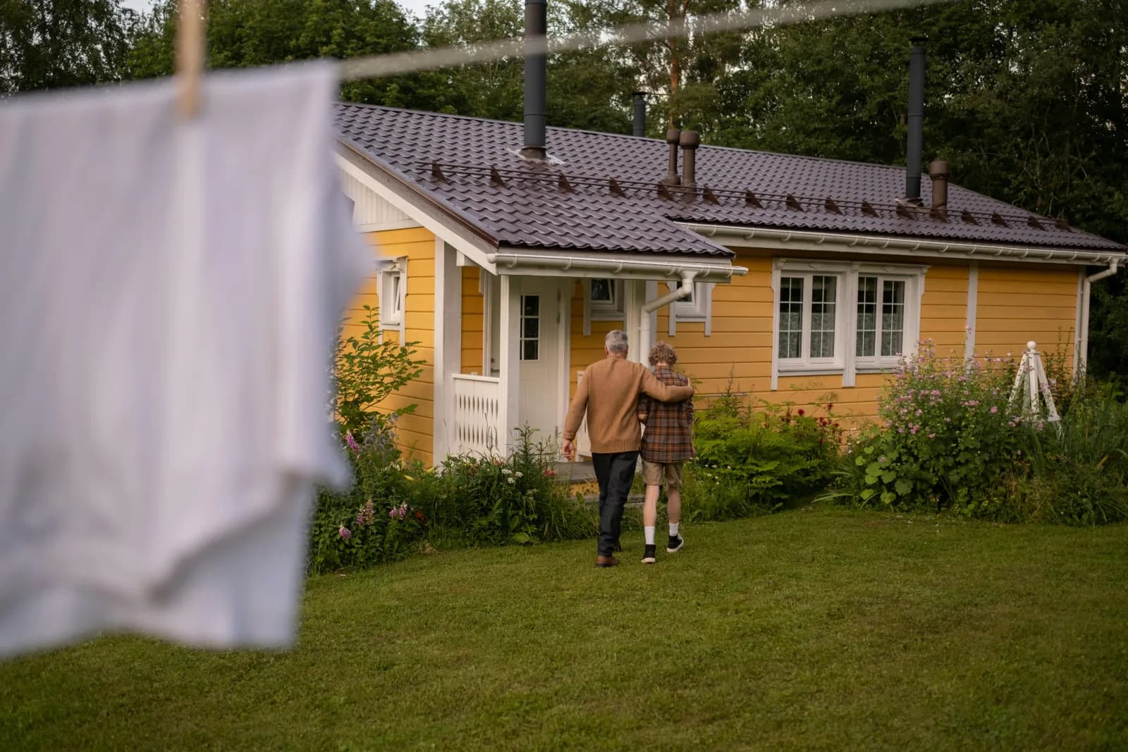 Person på vei mot et gult hus med hage i gyllent ettermiddagslys