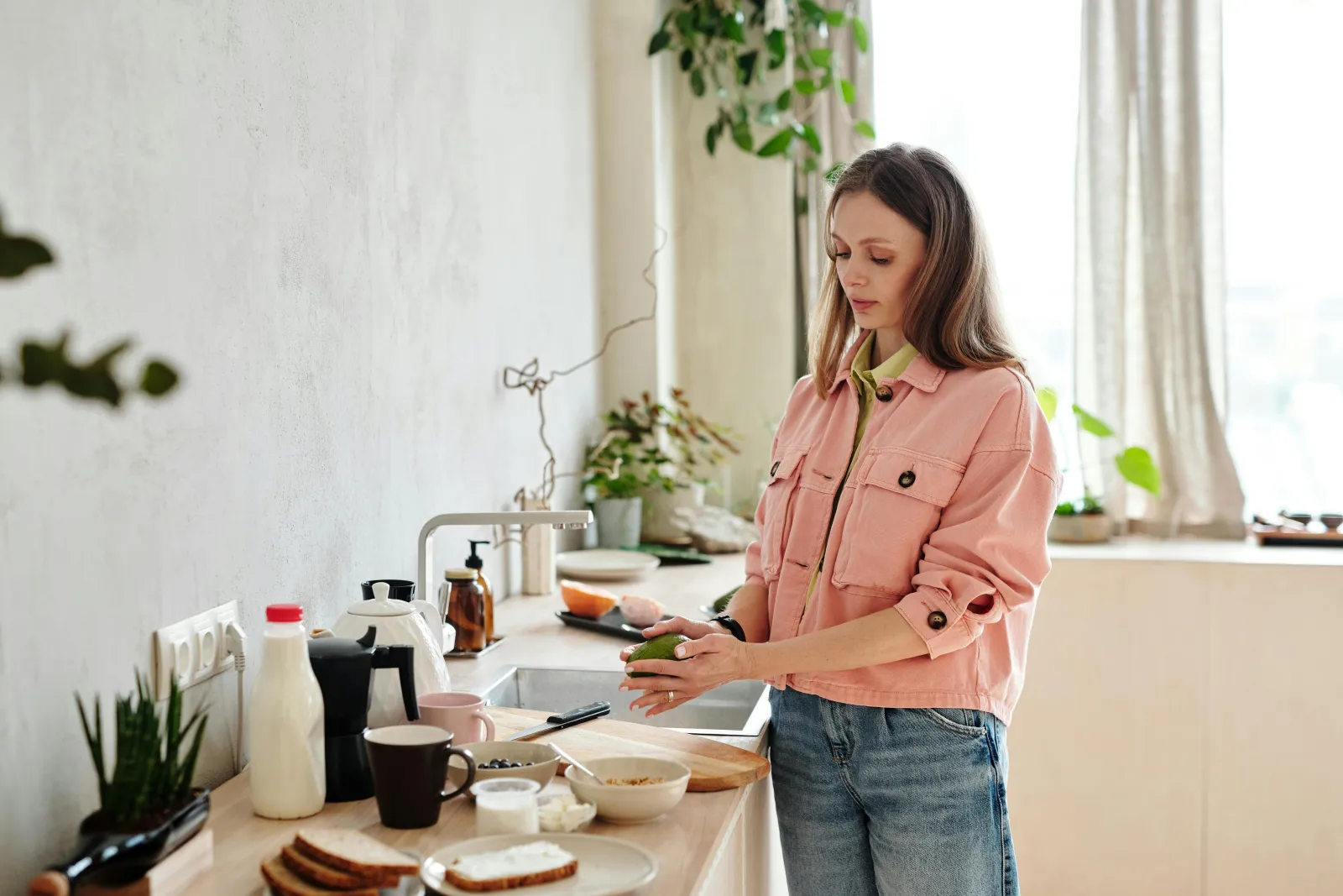 Lyst kjøkken med planter og kvinne ved vinduet i varmt dagslys