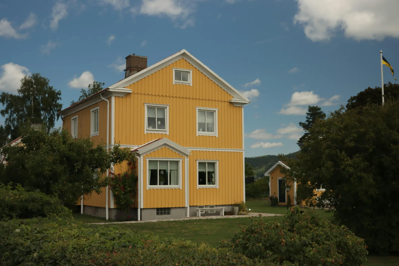 Gult trehus i et grønt landskap på landsbygda en sommerdag