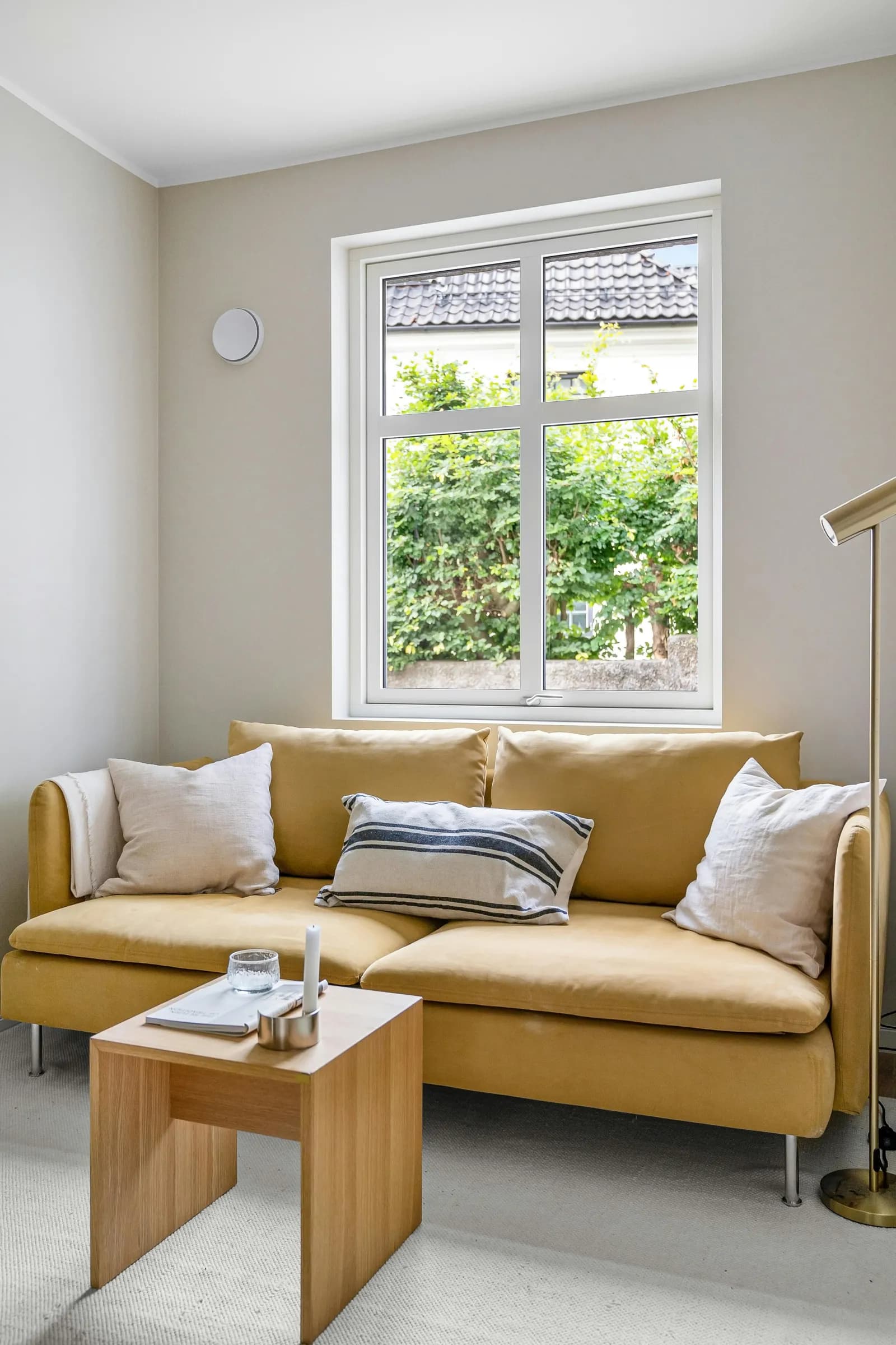 Stue med sennepsgul sofa, trepanel og planter i varmt dagslys